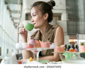 Mature Asian Woman Enjoying Afternoon Tea In Modern Hotel Restaurant