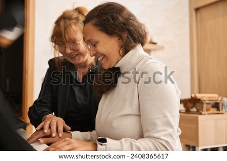 Mature Asian woman, female pianist, musician , music teacher putting her hand on student's hand, showing her position of fingers on piano keys during music lesson on chord instrument. Piano lesson