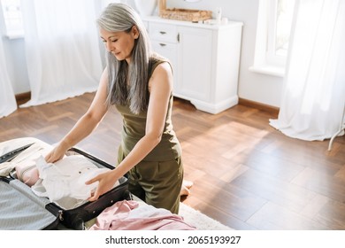 Mature Asian Woman With Grey Hair Packing Suitcase On Bed At Home