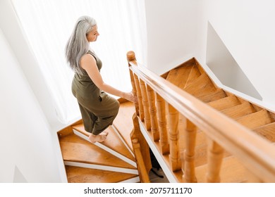 Mature Asian Woman With Grey Hair Going Up Stairs At Home