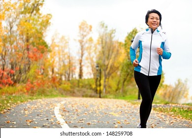 Mature Asian woman running active in her 50s. Middle aged female jogging outdoor living healthy lifestyle in beautiful autumn city park in colorful fall foliage. Asian Chinese adult in her fifties.
