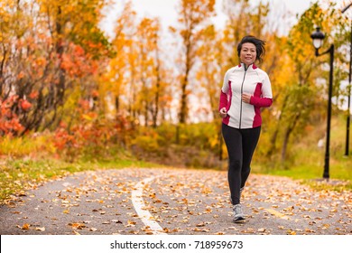 Mature Asian Woman Running Active In Her 50s. Middle Aged Female Jogging Outdoor Living Healthy Lifestyle In Beautiful Autumn City Park In Colorful Fall Foliage. Asian Chinese Adult In Her Fifties.