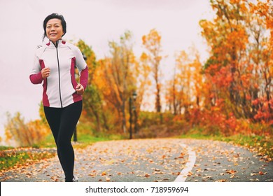Mature Asian woman running active in her 50s. Middle aged female jogging outdoor living healthy lifestyle in beautiful autumn city park in colorful fall foliage. Asian Chinese adult in her fifties.