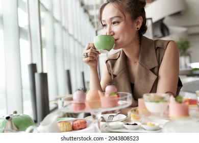 mature asian woman sitting at table eating dessert drinking tea in hotel lobby coffee shop