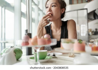 Mature Asian Woman Sitting At Table Eating Dessert Alone In Hotel Lobby Coffee Shop