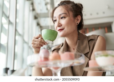 Mature Asian Woman Sitting At Table Having Afternoon Tea In Coffee Shop Of Luxurious Hotel