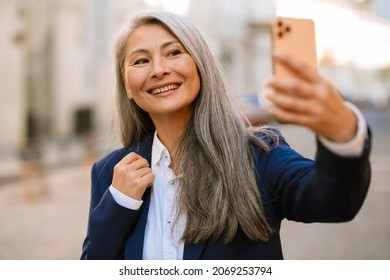 Mature Asian Woman Smiling And Taking Selfie On Mobile Phone Outdoors