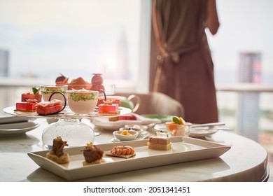 mature asian woman standing by the window looking at city view with food on table in a hotel room