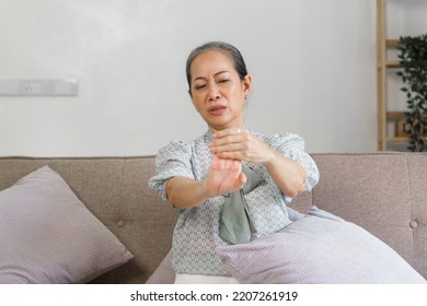 Mature Asian Woman Suffering From Pain In Hand, Sitting On Couch.