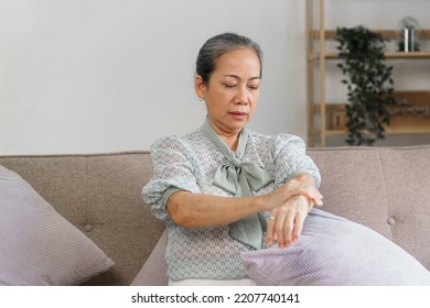 Mature Asian Woman Suffering From Pain In Hand, Sitting On Couch.