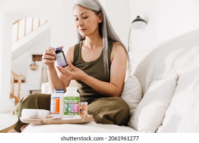 Mature asian woman taking her medication while sitting on couch at home