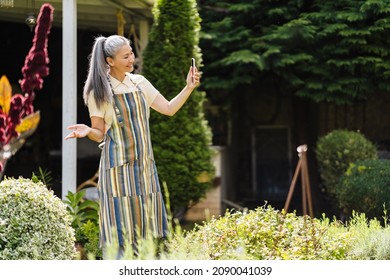 Mature Asian Woman Taking Selfie On Cellphone While Working In Her Garden