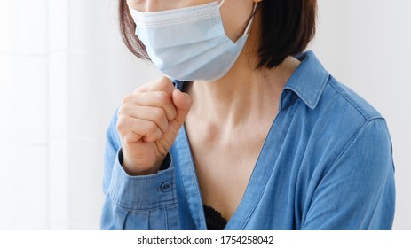 Mature Asian Woman Wearing Mask Coughing At Living Room