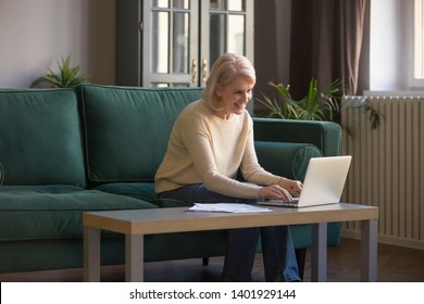 Mature Attractive Woman Sitting On Couch In Living Room Paying Bills Online Using E-banking Internet Application, Satisfied Elderly Female Working On Computer Spending Free Time Browse Website Concept