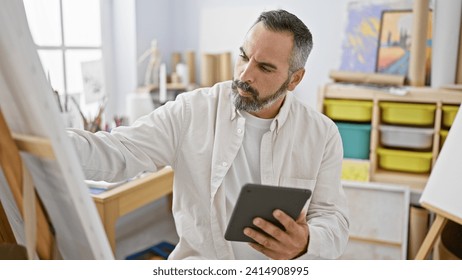 A mature bearded man with grey hair using a tablet in a bright art studio. - Powered by Shutterstock