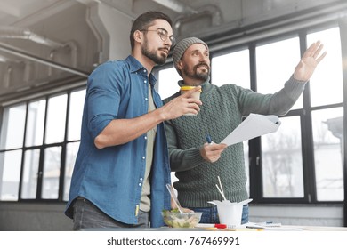 Mature bearded marketing director and his assistant choose place where conduct meeting with business patrners, points at spacious cabinet, have coffee break or lunch, prepare financial report