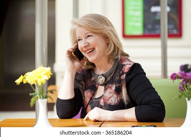 Mature beautiful blonde woman is calling on a cell phone while sitting in a coffee shop