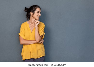 Mature beautiful latin woman isolated on grey background looking on side with copy space. Portrait of positive latin woman smiling. Happy middle aged lady standing against grey wall and thinking.
