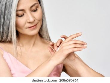 Mature Beautiful Senior Mid Age Older Asian Woman Of 50s Years Applying Putting Skin Care Lotion Hand Cream Doing Her Everyday Routine. Antiaging Beauty Skin Face Body Care Concept.