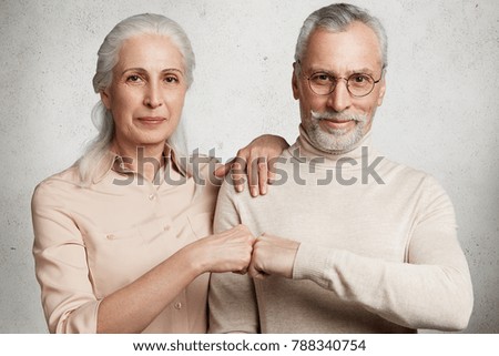 Mature beautiful woman and handsome bearded man express agreement, touch fists, isolated over white concrete background. Grandparents have good relationship, agree with something. Family and pension