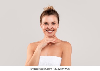 Mature Beauty. Portrait Of Attractive Middle Aged Woman Wrapped In Bath Towel Posing Over Light Grey Studio Background, Beautiful Female Touching Chin And Smiling At Camera, Copy Space