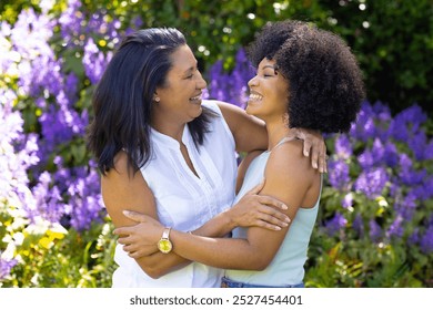 A mature biracial woman and her young daughter laugh and hug at home in garden. Wearing casual clothes, daughter with curly hair and mother with straight hair, both enjoying warm, sunny day surrounded - Powered by Shutterstock