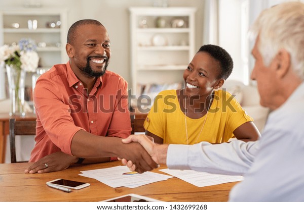 Mature black husband shaking hands with senior
agent on taking loan. Happy african couple sealing with handshake a
contract with financial advisor for investment. Man making sale
purchase deal.