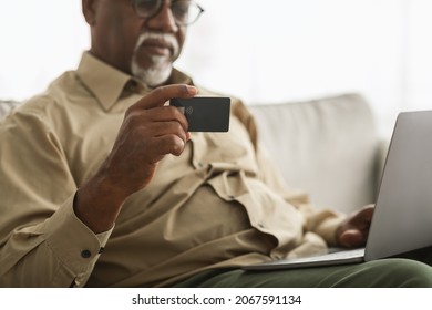 Mature Black Man Holding Credit Card Shopping Online Using Laptop Computer Sitting On Couch At Home. Cropped Shot, Selective Focus On Bank Card. Internet Banking And E-Commerce Concept