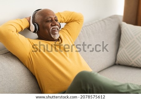 Mature Black Man Listening To Music Wearing Wireless Headphones And Holding Hands Behind Head Sitting On Couch At Home. Senior Male Relaxing Resting On Sofa Enjoying Favorite Song Stock foto © 
