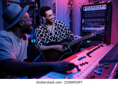 Mature Black Music Producer And Young Guitar Player Enjoying Working On Album In Recording Studio, Neon Lighting