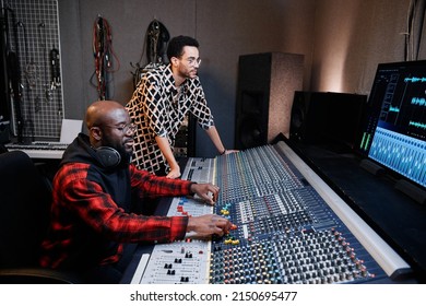 Mature Black Music Producer And Young Male Singer Working Together On Song In Recording Studio