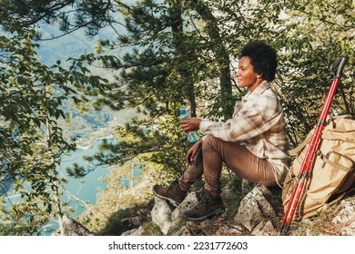 Mature black woman taking a water break and enjoying the view on the top a hill during hike in the mountains. - Powered by Shutterstock