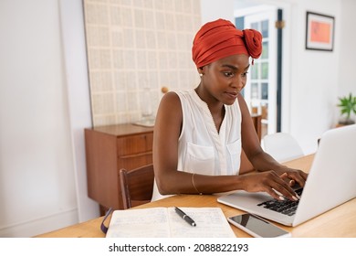 Mature Black Woman With Traditional Turban Sitting At Home While Working On Laptop. Successful Black Businesswoman Typing On Laptop Wearing A Traditional Turban While Working From Home With Copy Space