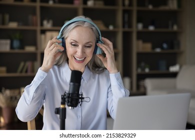 Mature blogger woman in headphones speaking at professional microphone at laptop, taking video for blog. Senior radio host, speaker holding program on air, broadcasting, recording audio book