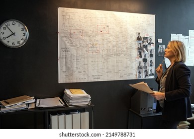 Mature Blond Serious Female Investigator Looking At Map On Board While Thinking Of Ideas About Possible Location Of Serial Killer