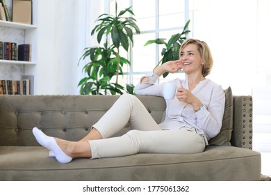 Mature Blond Woman In Couch Having A Tea Or Coffee.