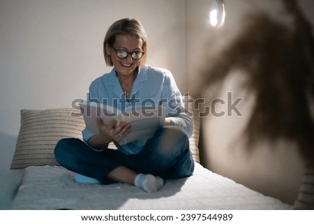 mature blond woman with glasses reads a book in the evening hours and rests