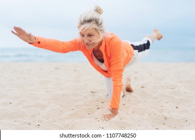 Mature blond woman working out doing yoga exercises on a sandy tropical beach on an overcast day in a close up low angle frontal view - Powered by Shutterstock