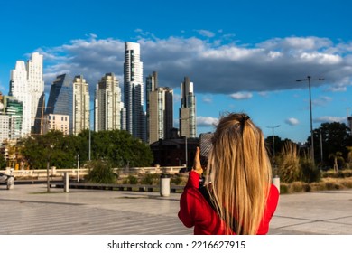 Mature blonde adult woman taking a smartphone photo of a group of buildings in the Puerto Madero area, Buenos Aires.