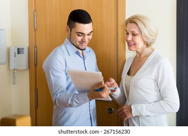 Mature Blonde Woman Answer Questions Of Smiling Guy With Papers At Door In Home 
