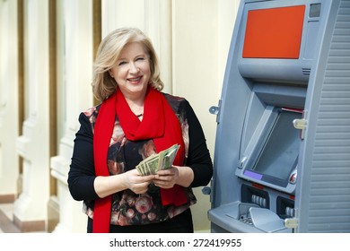 Mature Blonde Woman Counting Money Near Automated Teller Machine In Shop