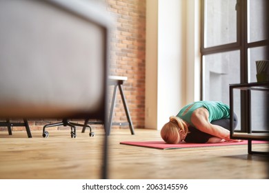 Mature Blonde Woman Practicing Yoga At Home, Sitting In Child Pose, Balasana On The Floor In Modern Apartment