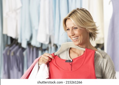 Mature Blonde Woman Shopping In Clothes Shop, Holding Red Vest Top On Coathanger, Smiling
