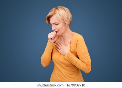 Mature Blonde Woman Standing Isolated On Blue Background Coronavirus Concept Coughing Touching Chest Wincing From Pain