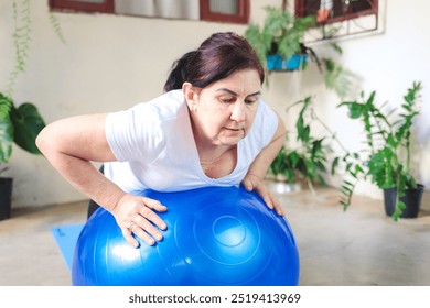 Mature Brazilian woman doing exercises at home with a stability ball. Promoting a healthy lifestyle through simple home workouts that enhance physical and mental well-being - Powered by Shutterstock