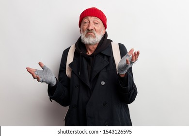 Mature Bum, Homeless Old Man With Grey Beard In Coat And Red Hat Shrugs Isolated Over White Background