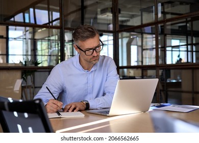 Mature business man executive manager looking at laptop computer watching online webinar training having virtual meeting video conference taking notes  doing market research working in office 