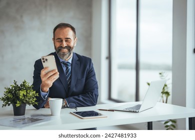 Mature business man in formal clothing wearing spectacles using mobile phone. Serious businessman using smartphone and digital tablet at work. Manager in suit using cellphone in a modern office. - Powered by Shutterstock