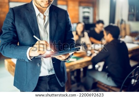 A mature business manager smiling confidently looks at the camera standing in the office at a team meeting. Male corporate leaders, CEOs, and senior Asian executives wearing glasses pose for business 