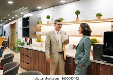 Mature business people standing in office kitchen, drinking coffee and discussing news and gossips